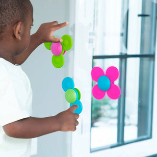 Child playing with colorful flower-shaped window stickers on a glass door.