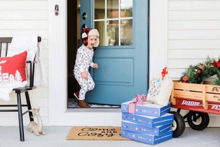 Child in festive outfit standing on a porch with Christmas decorations