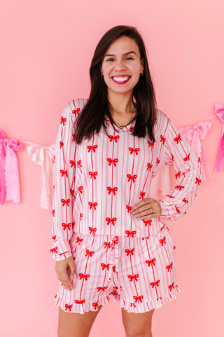 Woman wearing a pajama set with red bow pattern against a pink background