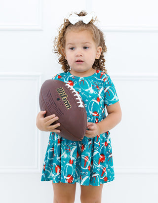 Child wearing a blue dress with football pattern holding a Wilson football against a white background