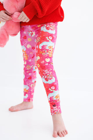 Child wearing colorful leggings with a red sweater and pink care bear on a white background