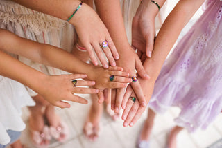 Children's hands with painted nails wearing rainbow metallic smiley face rings held together in a circle