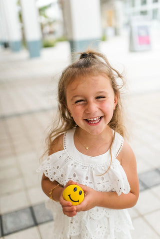 Young girl wearing a solid heart shaped pendant necklace while holding a yellow smiley face ball