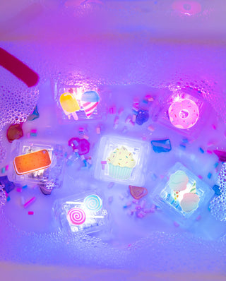 Colorful light up cubes with various shapes and designs floating in a bathtub filled with water and bubbles.