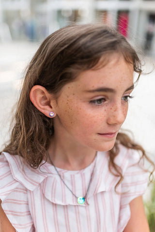 Young girl wearing a stainless steel rainbow metallic necklace and matching smiley face earrings with a blurred background