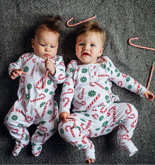 Two babies wearing pajamas with candy cane patterns on a gray carpet.