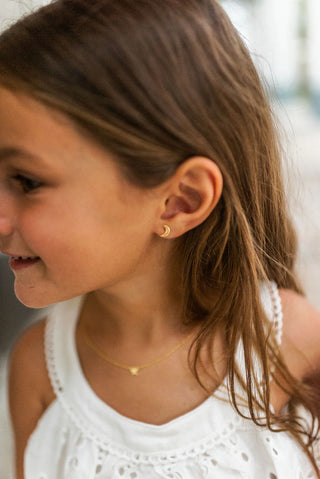 Close-up of a young girl wearing gold moon earring and a necklace.