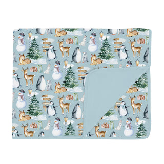 folded blanket with winter-themed design featuring animals and trees on a light blue background.