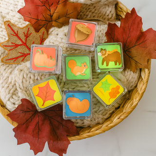 Set of colorful water activated light up cubes with autumn-themed designs in a basket with leaves and yarn.