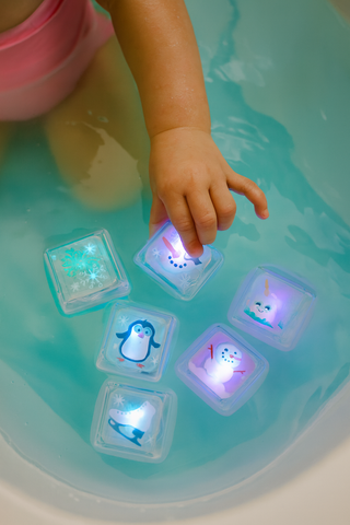 Child's hand interacting with glowing ice cube toys in a bathtub