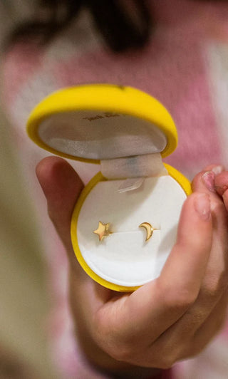 Gold star and moon earrings in a yellow case held by a hand.