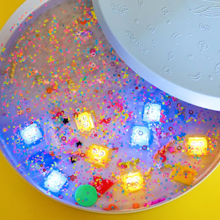 Colorful water activated light up cubes with embedded toys and sprinkles on a yellow background