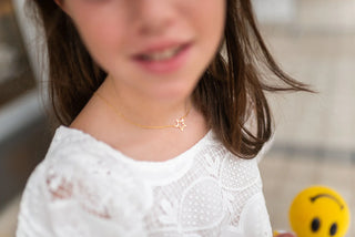 Close-up of a child wearing a gold necklace with a star pendant, blurred background