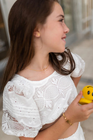 Girlin a white lace top holding a yellow rubber duck wearing a gold star pendant necklace.