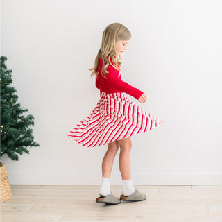 Young girl in a red top and red and white striped skirt standing next to a Christmas tree.