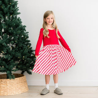 Young girl in a red top and striped skirt standing next to a Christmas tree.