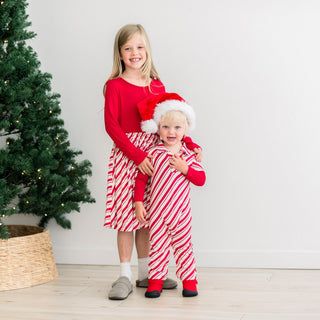 Two children in red and white striped outfits standing in front of a Christmas tree.