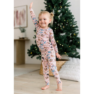Child wearing a pink pajama set with animal print in a room with a decorated Christmas tree.