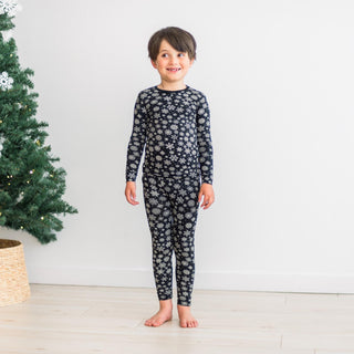Child wearing snowflake pajama set standing in front of a decorated Christmas tree.