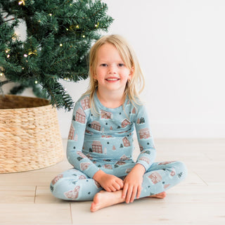 Child wearing festive pajamas with gingerbread houses on them sitting in front of a decorated Christmas tree.