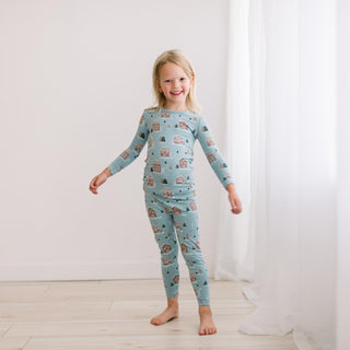Child wearing a blue pajama set with gingerbread house print in a bright room.