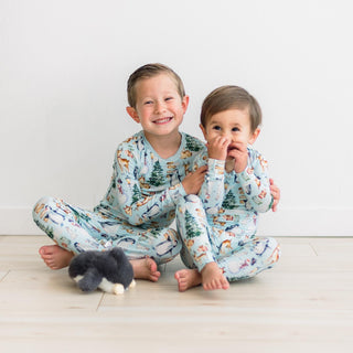 Two children wearing matching pajamas with a winter wonderland design on a light wooden floor.