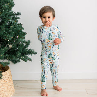 Child wearing a winter wonderland-themed pajama set standing next to a decorated Christmas tree.
