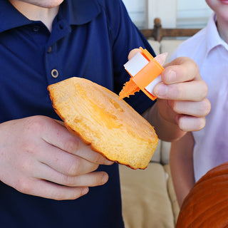 Person using a tool to attach an LED light to the inside top of a pumpkin.