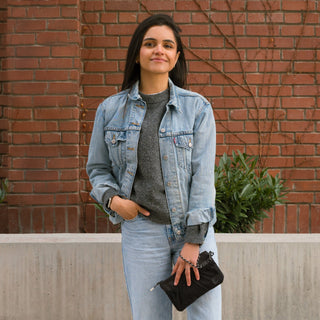 Woman wearing a denim jacket and jeans standing against a brick wall.