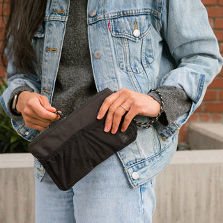 Person holding a black pouch with a brick wall background