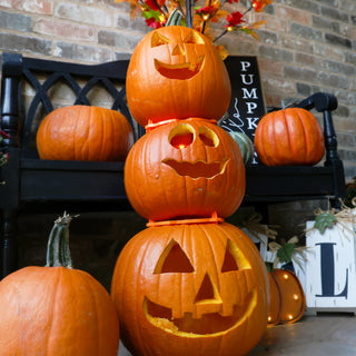 Stack of carved pumpkins with a black bench and brick wall in the background