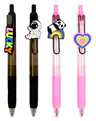 Four retractable gel pens arranged upright on a white background, each with a different decorative clip: a colorful 'LUCKY' text clip, an astronaut clip, a panda and rainbow clip, and a heart-shaped clip.