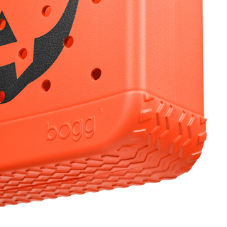 Close-up of an orange pumpkin-themed tote with a black jack o lantern design, featuring the brand 'bogg'.